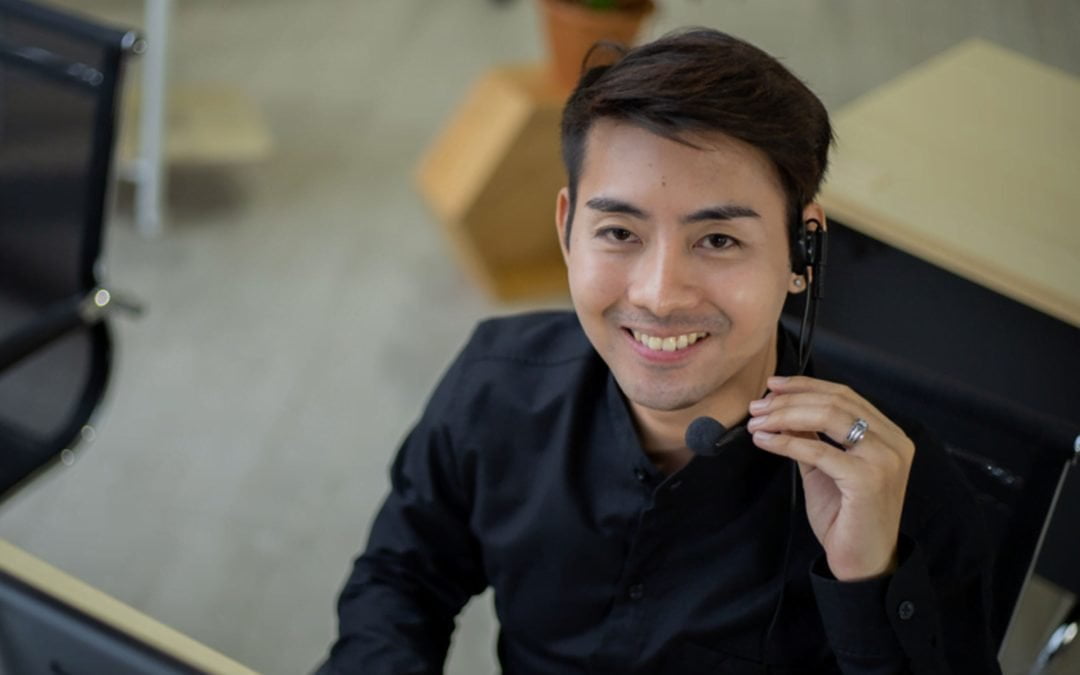 Contact Center Agent senyum ke kamera dengan menggunakan headphone